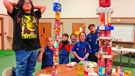 The Webelos Den of Pack 131 with the two stacks of food they collected for the Leelanau Christian Neighbors Food Pantry. One stack measured 46 inches high, the other stack measured 38 inches high.Webelos Scouts who participated were Wamigo Winchester in front and from left Beau Underhill,...