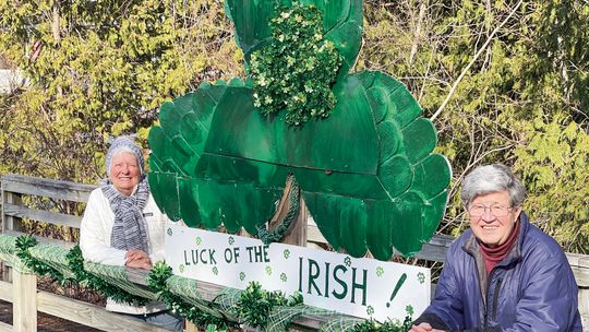 Judy Walter (left) and her husband, Jon, have been decorating the bridge off Elm Street in Suttons Bay since last July. Their latest creation, a giant green shamrock for St. Patrick’s Day, is on display for those passing by to see. Enterprise photo by Meakalia Previch-Liu