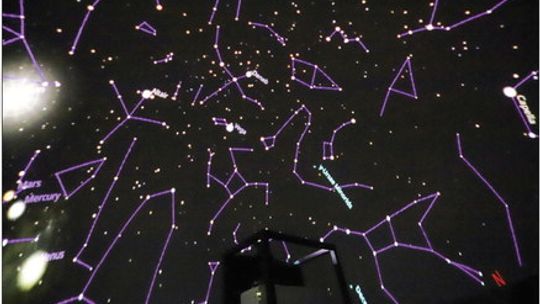 A view of the ceiling inside Sleeping Bear Dunes National Lakeshore’s new inflatable planetarium dome. A projection of the night sky is visible with outlines of constellations and labels of major celestial bodies. The vertical projector is visible in the foreground. Photo courtesy of the N...