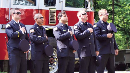 Members of the Glen Lake Fire Department salute the flag at last year’s flagraising ceremony organized by the Glen Lake Woman’s Club. Photo courtesy of Grace Dickinson Johnson