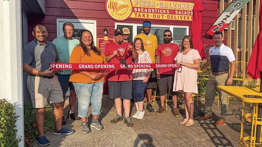 Suttons Bay community members gather to cut the ribbon during a grand opening for Bay Pizzeria Monday. Courtesy photo