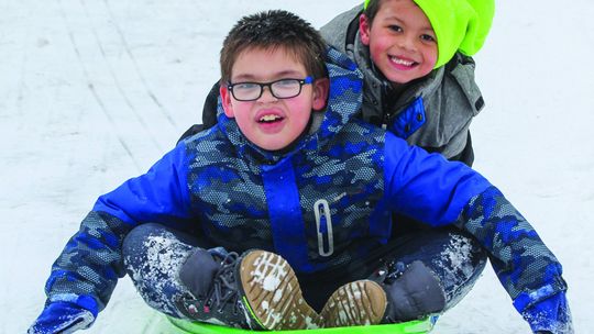 Nobody enjoyed the snow more than several Suttons Bay second graders that had some fun during recess last week. Declan Chippewa-Gillard (left), Gabriel Harper (right) share a thrilling ride on the playground. Enterprise photo by Brian Freiberger
