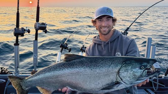 First mate Austin Rubin, a NMC student, holds a 24-pound salmon hooked by charter fisherman Adam Collett as the sun rises over the Manitou Passage. Courtesy photo