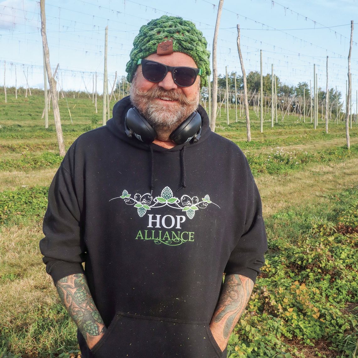 Hop Alliance owner Brian Tennis stand in his Omena Hop Yard earlier this month. Enterprise photo by Brian Freiberger