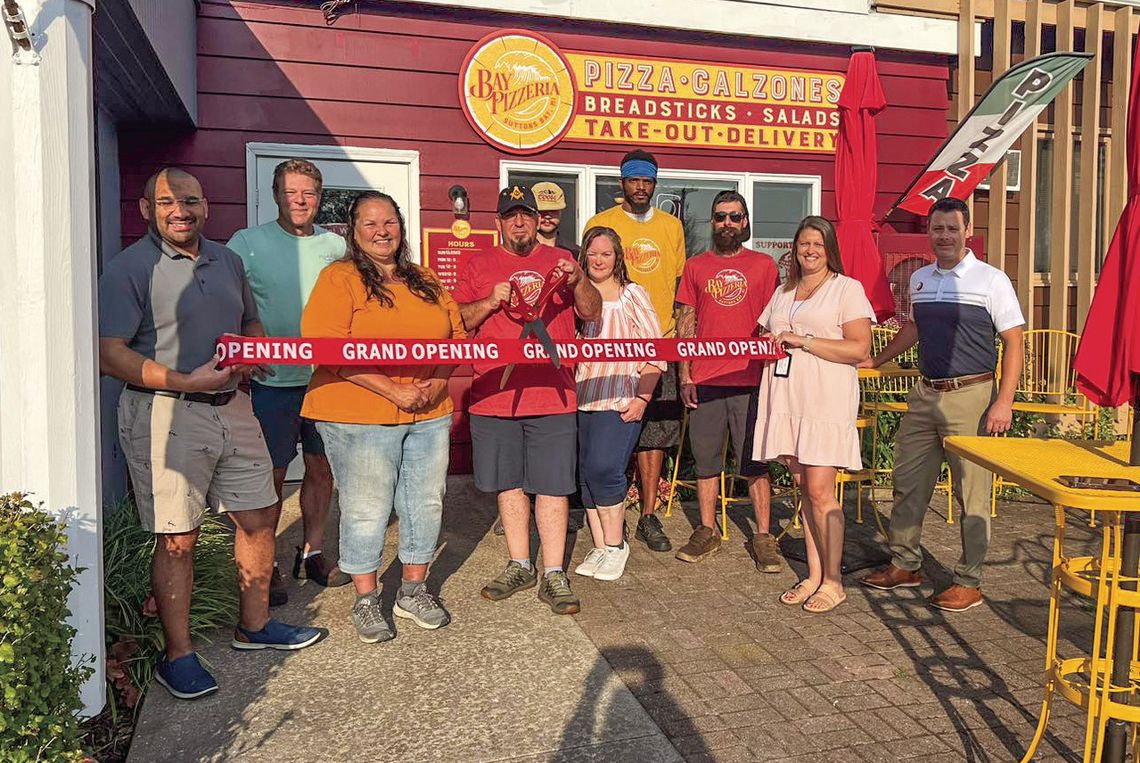 Suttons Bay community members gather to cut the ribbon during a grand opening for Bay Pizzeria Monday. Courtesy photo