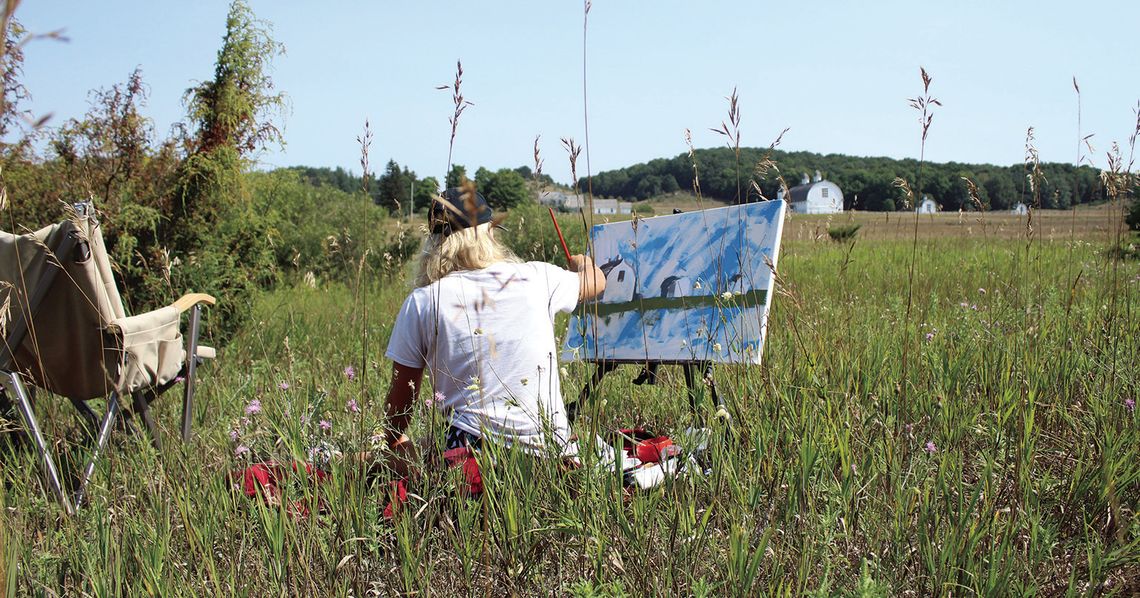 Mary Miller sits on a picnic blanket as she paints the DH Day Farm, a landmark at the Sleeping Bear Dunes National Lakeshore. Miller was one of 75 artists to participate in the 2024 Plein Air Paint Out hosted by the Glen Arbor Arts Center Saturday, where artists had just one day to fill a...