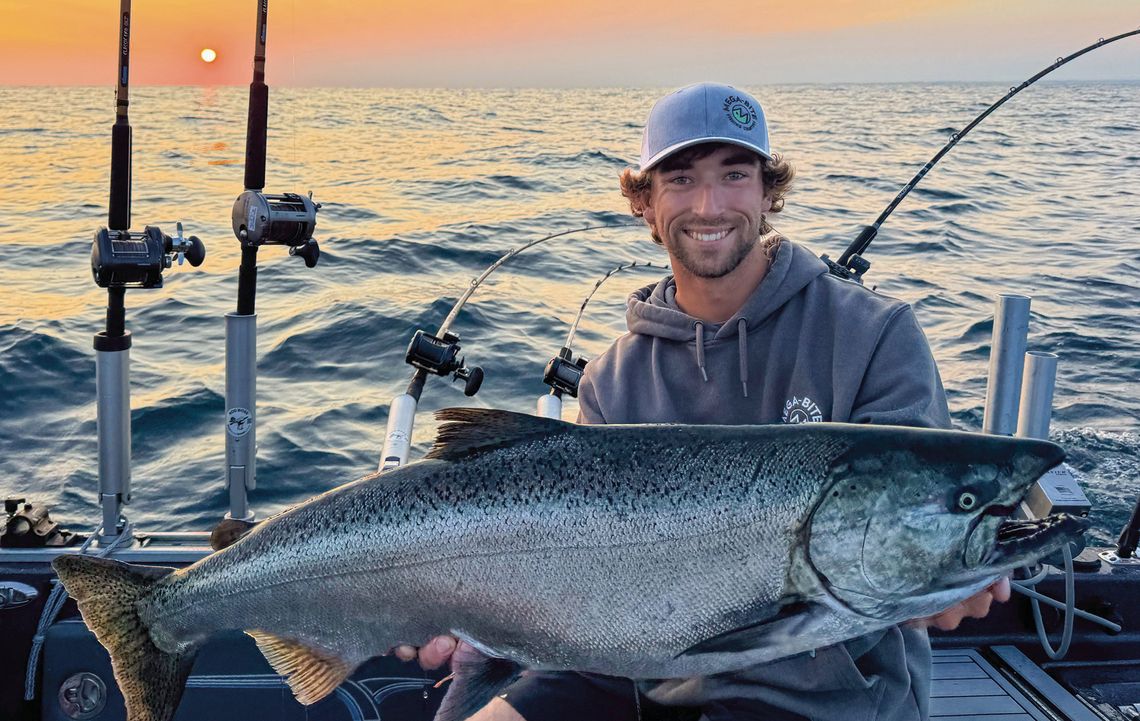 First mate Austin Rubin, a NMC student, holds a 24-pound salmon hooked by charter fisherman Adam Collett as the sun rises over the Manitou Passage. Courtesy photo