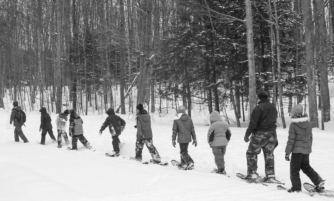 A school group snowshoes behind a ranger through a snowy forest at Sleeping Bear Dunes National Lakeshore. Photo courtesy of the National Park Service