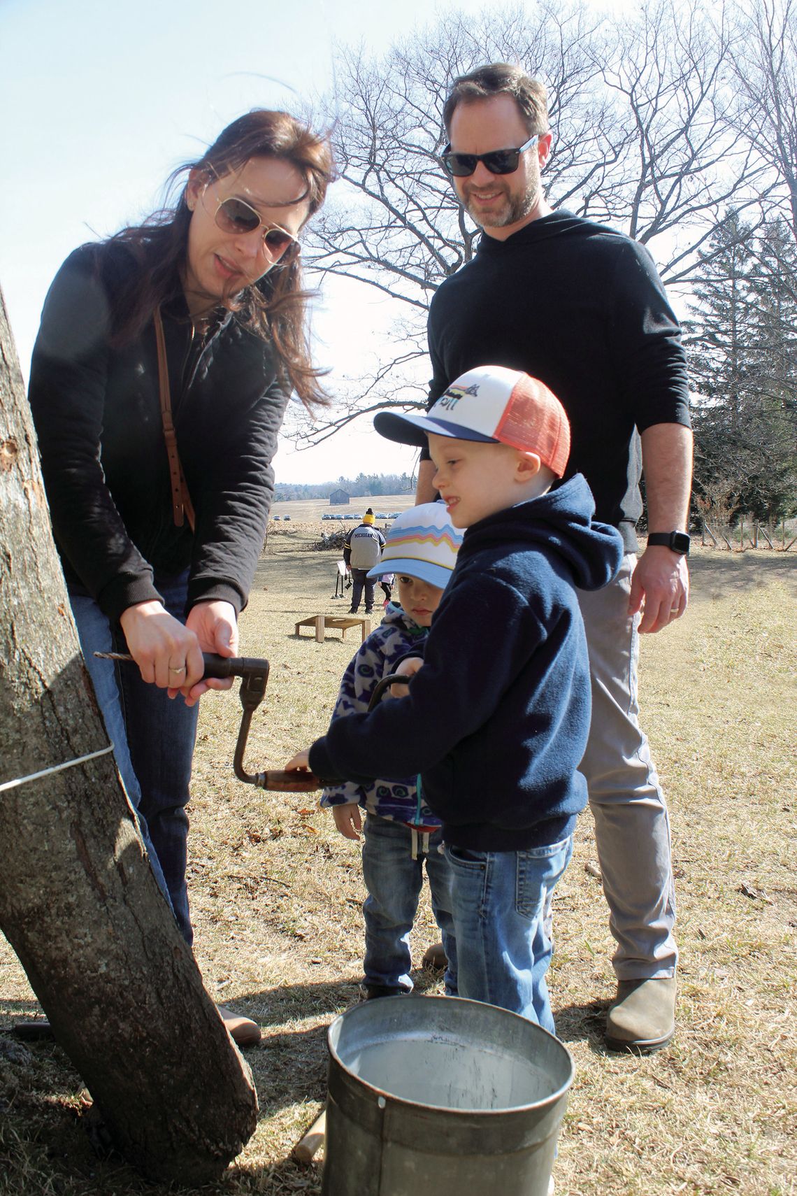 The LeRose family had a blast at Maple Sugaring Days at Dechow and Oleson family farms in the Port Oneida Rural Historical District on Sunday. Emily (left) helps Graham gather maple sap while his brother Hudson and father Claude watch. Enterprise photo by Brian Freiberger